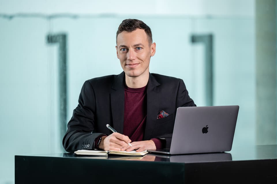 Adrian Ley am Schreibtisch, freundlich in die Kamera blickend